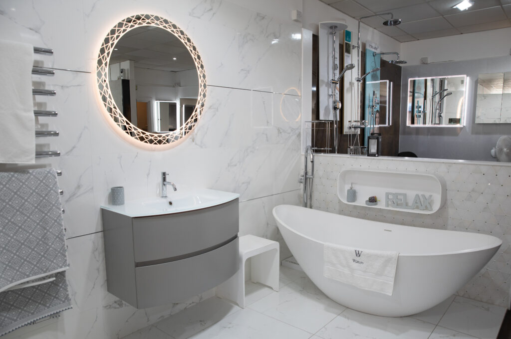 A white bathroom with a lit rounded mirror, designed by The Bathing Machine based in Caterham Valley
