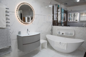 A white bathroom with a lit rounded mirror, designed by The Bathing Machine based in Caterham Valley